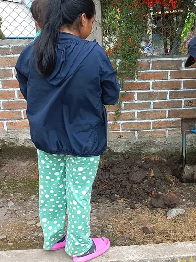 Photo of a worker digging a hole in front of a residence in Ecuador with an onlooker nearby
