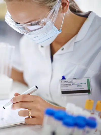 Photo of a woman scientist in a laboratory using a tablet to take notes