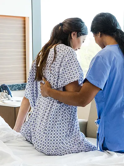 Nurse assisting woman sitting up in hospital bed