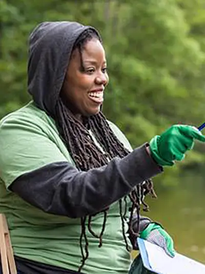 Women with wearing rubber gloves with community members cleaning up the shore of a lake