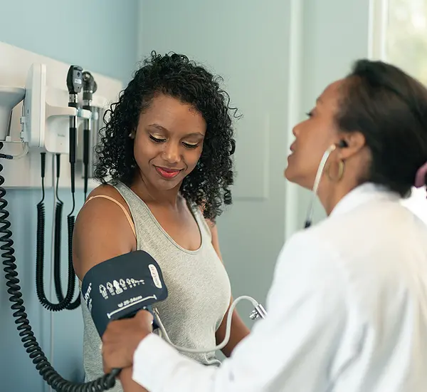 An African-American woman has her blood pressure checked by a female doctor.