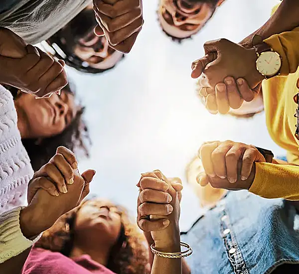 People holding hands in a circle, viewed from below, with the sky in the background.