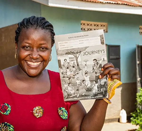 Rachel Nabbanja, a teacher at Kiiya Primary School in Luwero, Uganda, poses for a portrait with classroom material developed through Journeys. Photo: Katie G. Nelson for RTI International