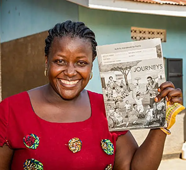 Rachel Nabbanja, a teacher at Kiiya Primary School in Luwero, Uganda, poses for a portrait with classroom material developed through Journeys. Photo: Katie G. Nelson for RTI International