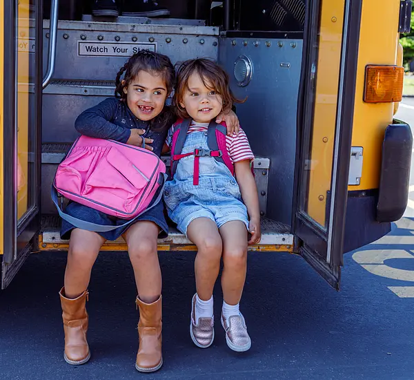Child with down syndrome sitting on school bus steps with friend