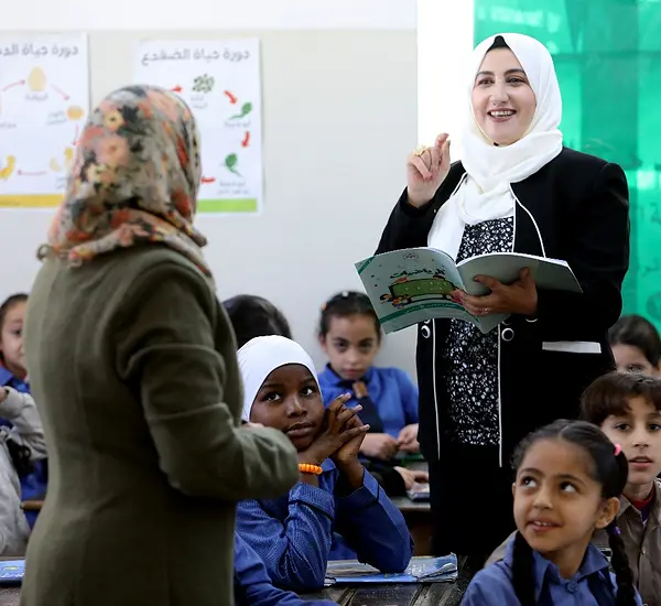 An educational supervisor checks in with a teacher in a classroom in Jordan.