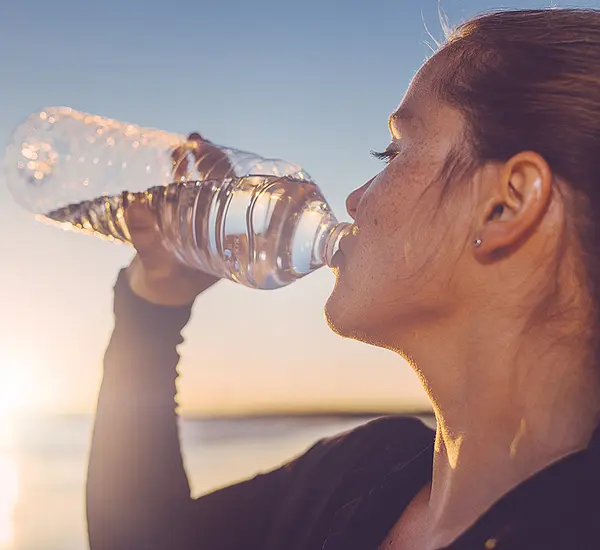 A woman drinks water from a clear disposable plastic water bottle.