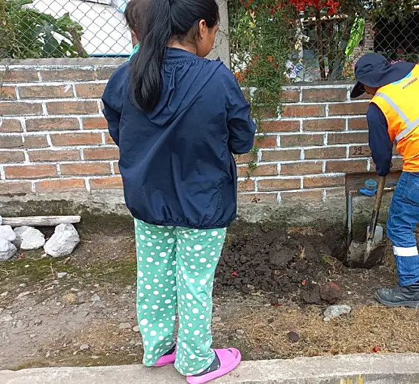 Photo of a worker digging a hole in front of a residence in Ecuador with an onlooker nearby