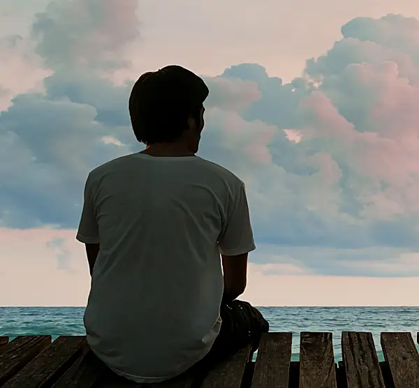 A solitary man watches the sun rise over the ocean from a pier.