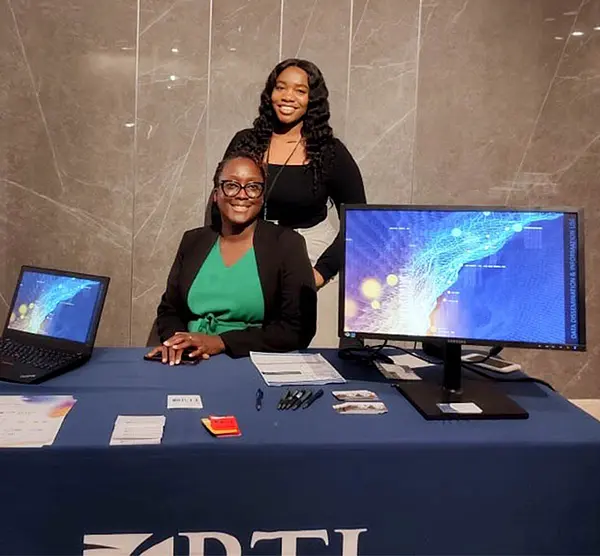 Rita Sembajwe and Shanice Fezeu Meyou pose in front of RTI’s booth at the 2022 DHIS2 Symposium.