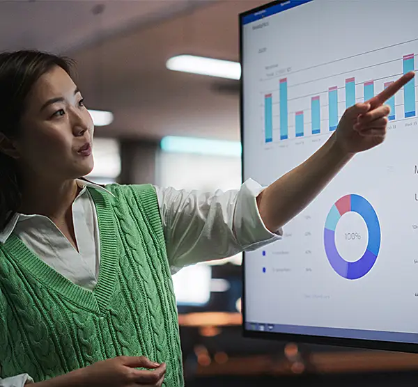 A woman points out graphs on a large monitor.