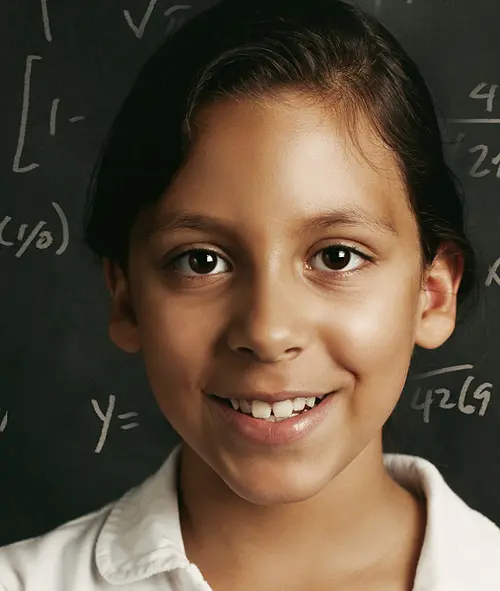 A young student in front of a chalkboard with equations written on it