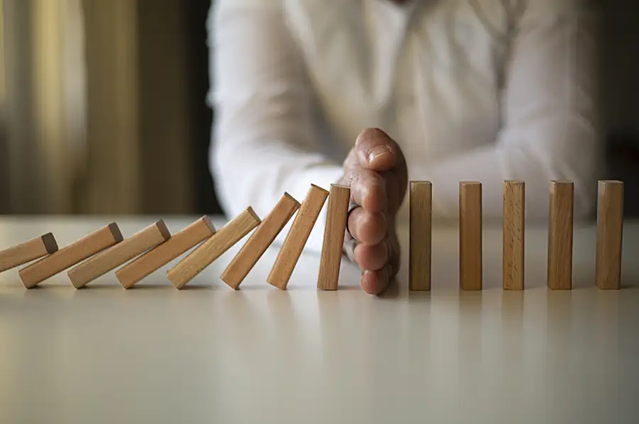 Photo illustration of a hand stopping a line of blocks from falling on each other.