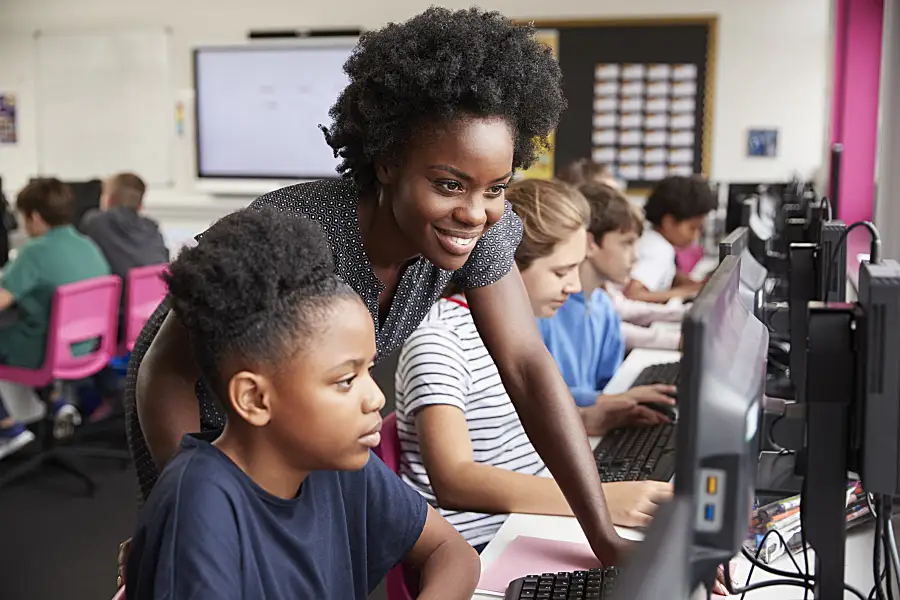 Teacher Helping Female Pupil Line Of High School Students Working at Screens In Computer Class