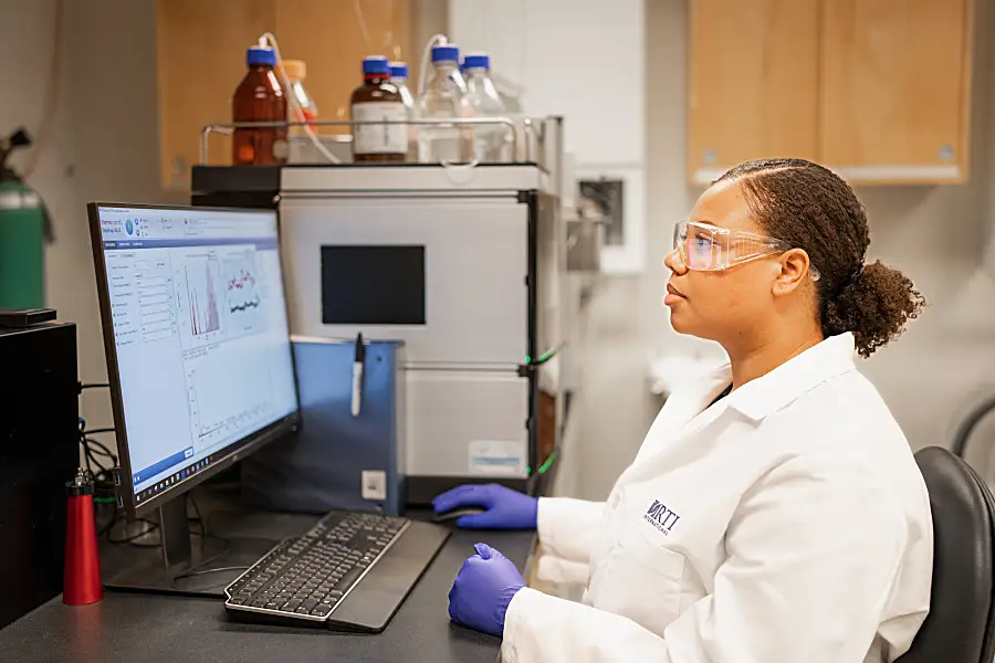 Imari Walker-Franklin wearing a lab coat sitting at a computer with data on the screen