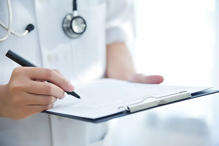 A closeup of a doctor in a lab coat checking items off of a list on a clipboard.