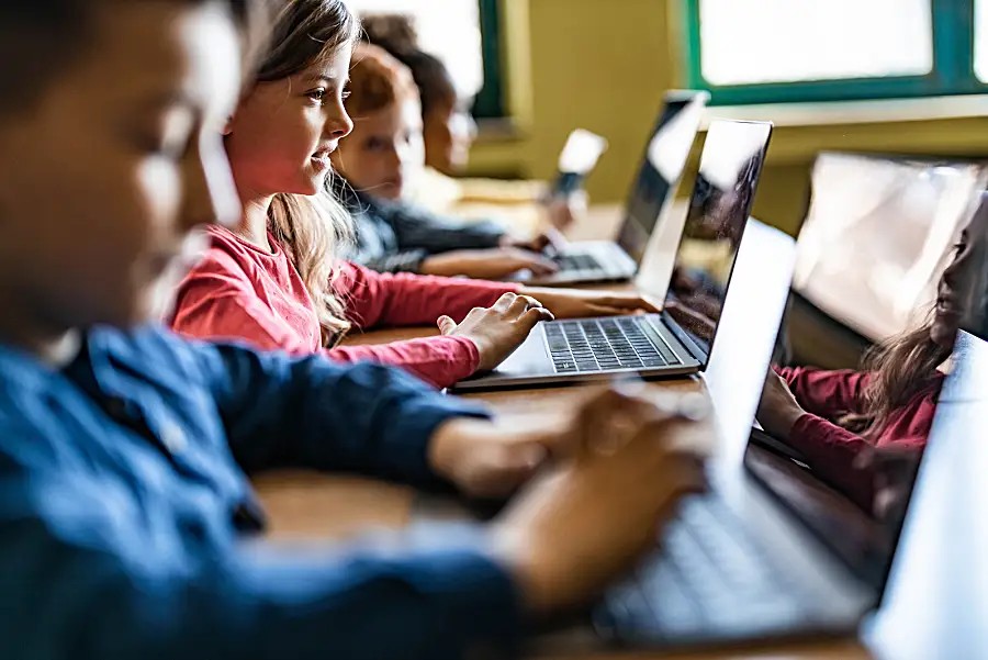 Children play educational games on laptop computers in a technology classroom. 