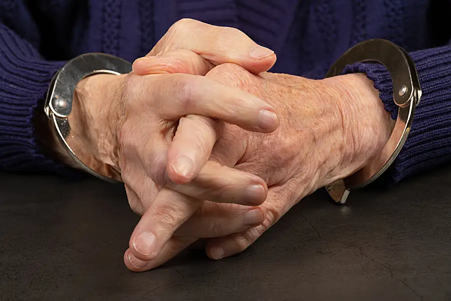 A closeup photo of a senior man's hands in handcuffs.