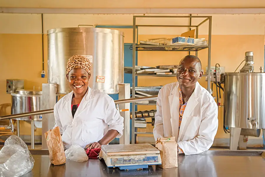 An African woman and man in white coats smiling in front of equipment