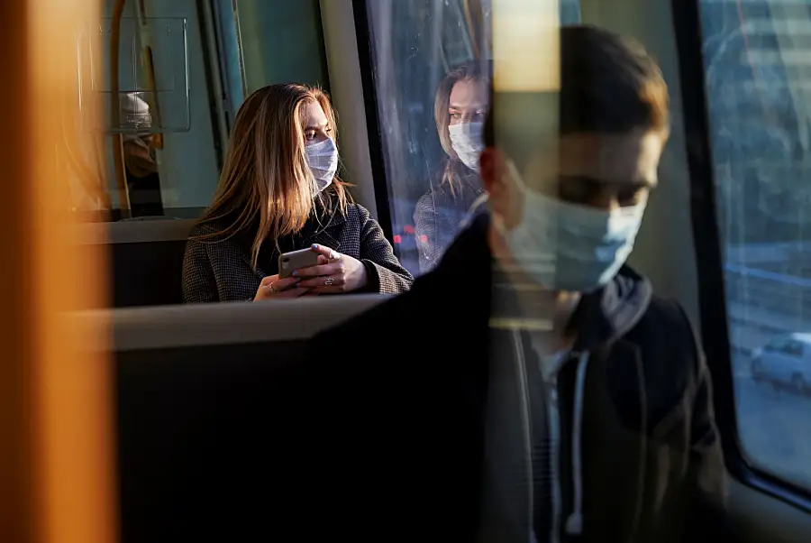 Woman wearing a protective medical mask staring out the window of a bus