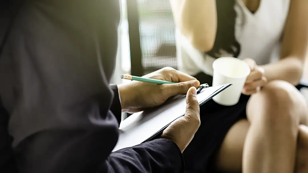 Closeup of a researcher taking notes on a clipboard while interviewing someone.