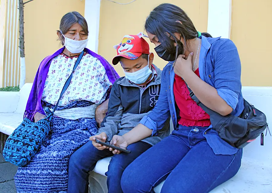 Photo of three people in Guatemala sitting outside together and looking at one of their phones