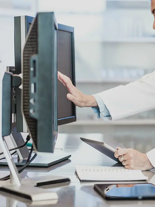 A female scientist in a white lab coat works with a touchscreen computer.