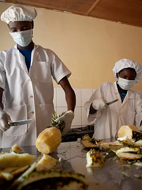 Rwandan food workers slicing pineapples