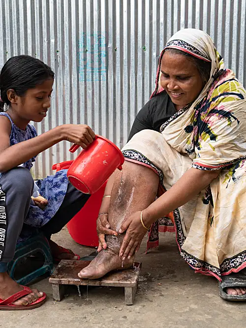 young girl helps wash an elder in Bangladesh