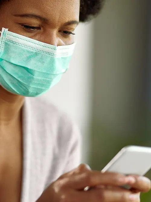 A woman wearing a surgical mask reads an article on a smartphone.
