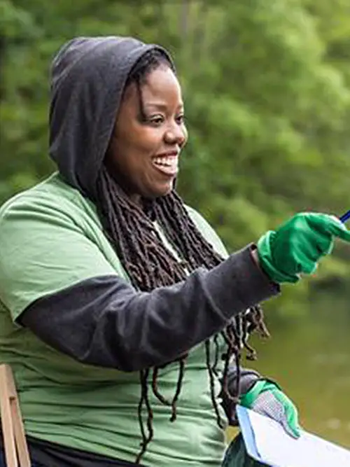 Women with wearing rubber gloves with community members cleaning up the shore of a lake