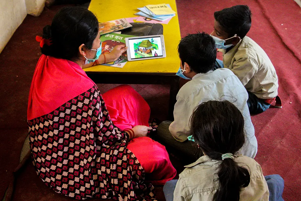 Students in the Nepal Early Grade Reading Program work with a teacher to practice reading skills on a tablet.