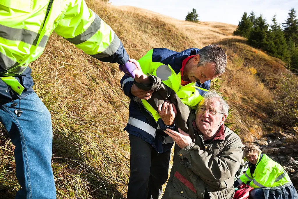 Rescuers help a senior man after a hiking accident on a mountain trail.