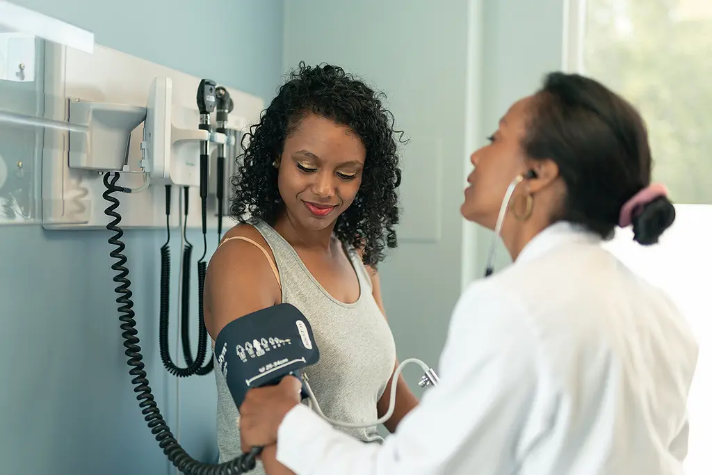 An African-American woman has her blood pressure checked by a female doctor.