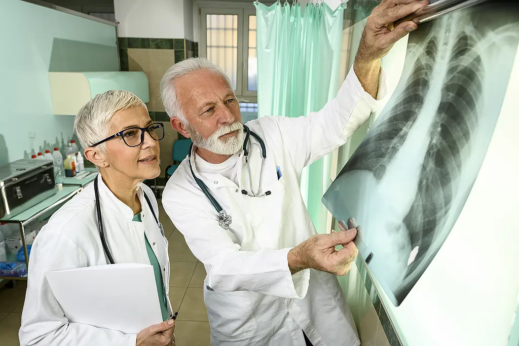 A male and female doctor, wearing lab coats, examine a set of chest x-rays.