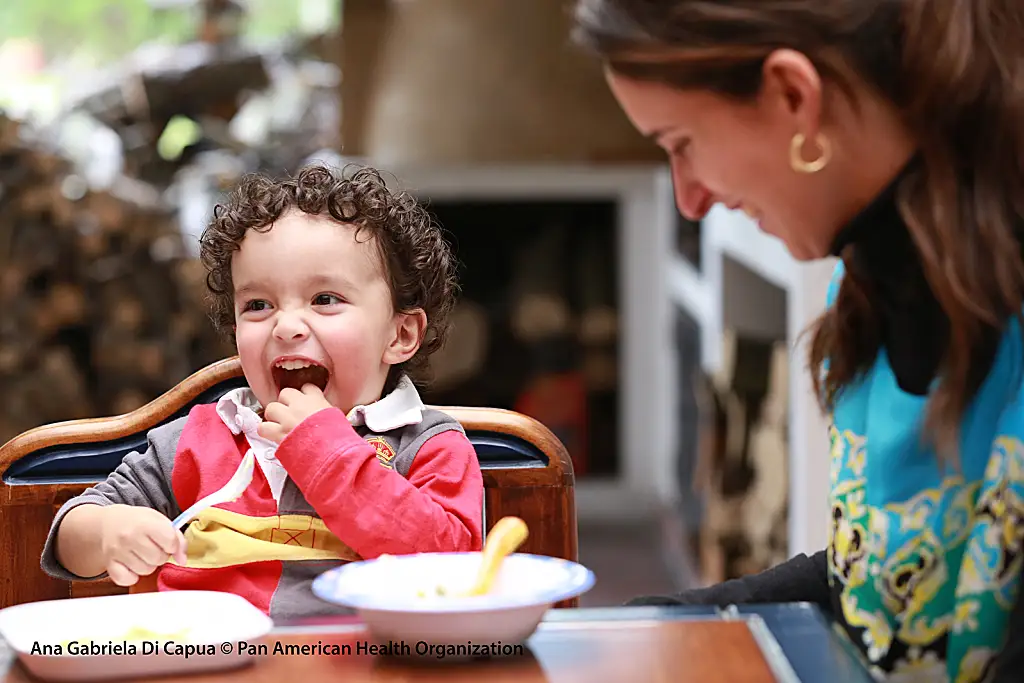 A mother and toddler eat at a table.