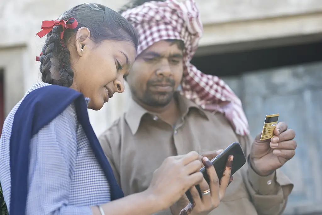 A young Indian woman with a smartphone helps a man use a credit card for a mobile payment.