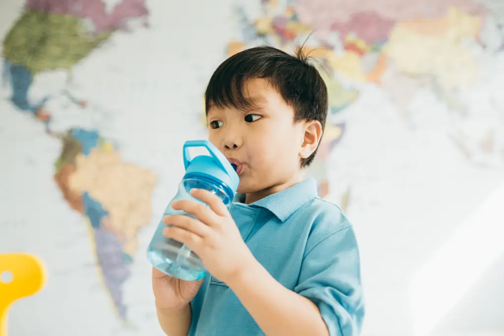A young Asian child drinking from a water bottle in front of a map