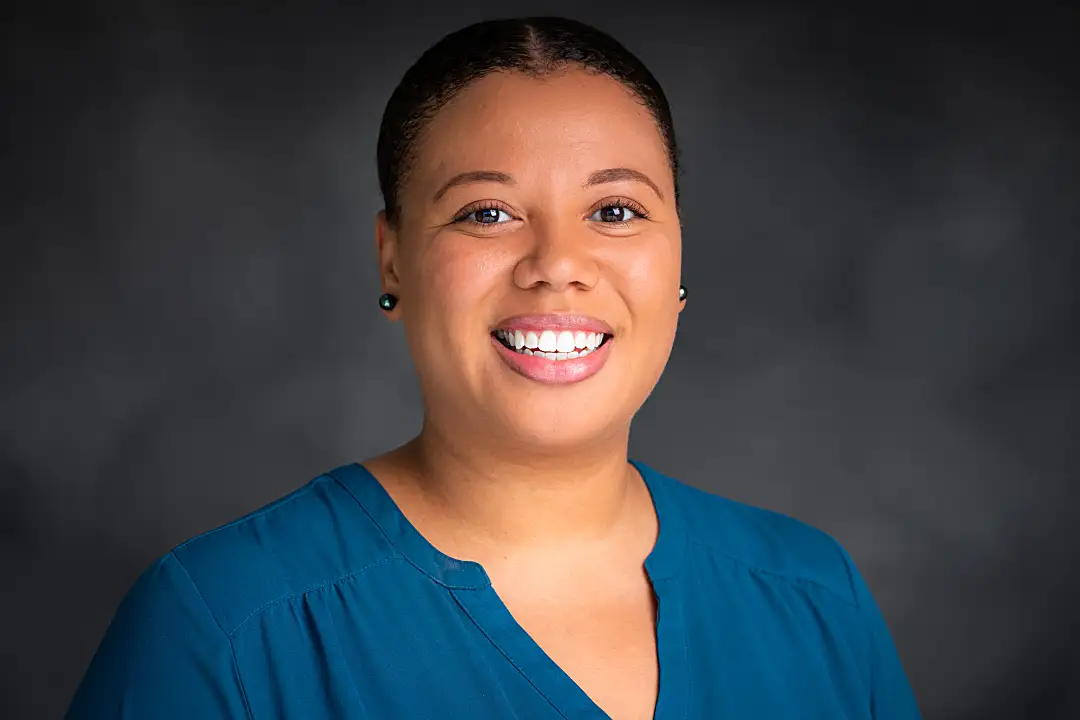 Headshot of Imari Walker-Franklin smiling against a dark background