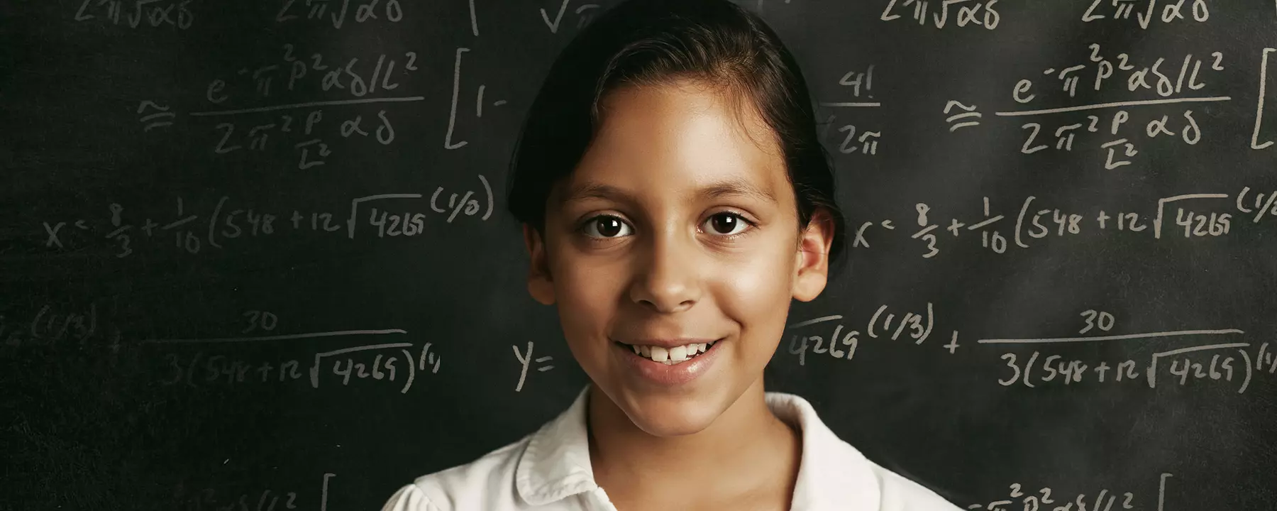 A young student in front of a chalkboard with equations written on it