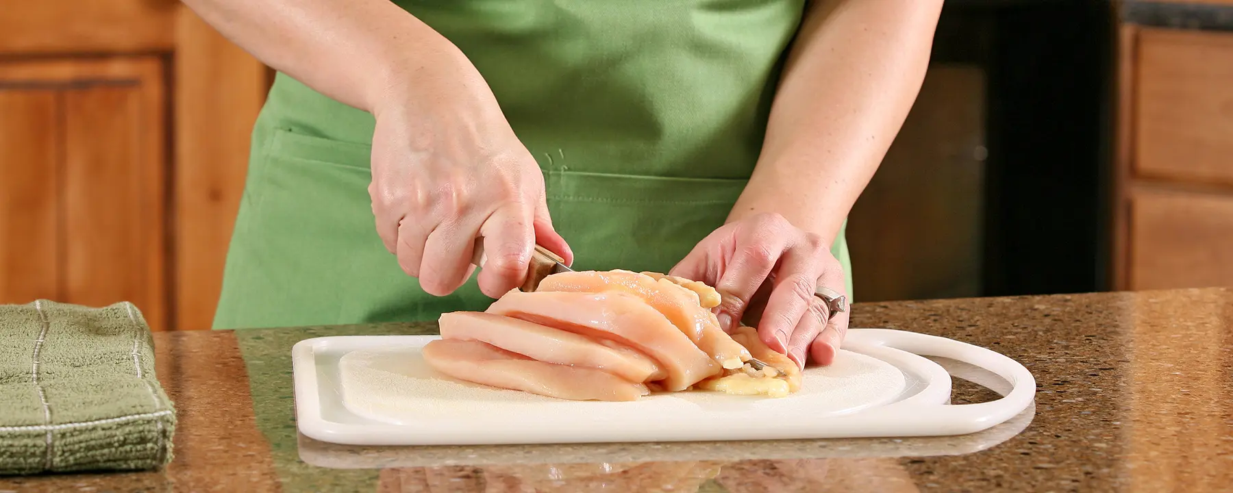 A closeup of a woman slicing raw chicken breast on a cutting board.