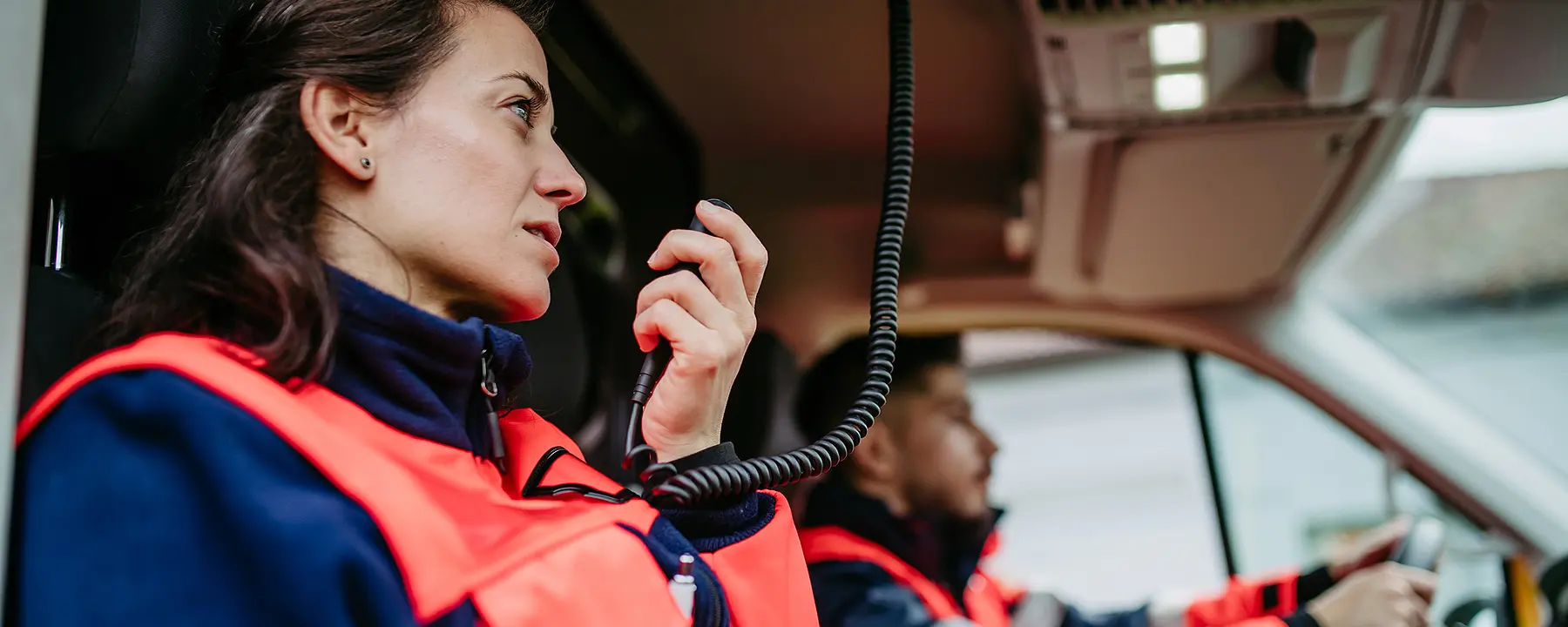 A female first responder talks on a handheld radio as her colleague drives the ambulance.