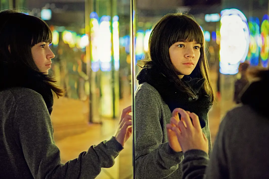 A young woman shown from two angles touching a mirror