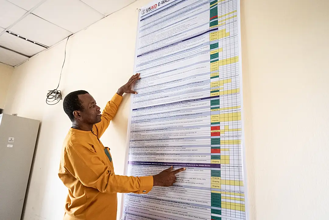 Photo of a Nigerian man smiling while pointing to a poster containing project data