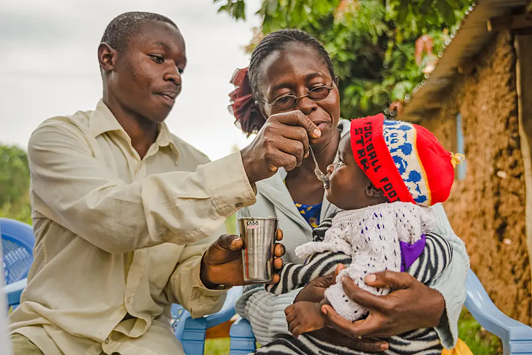 African parents feed a small child with a spoon.