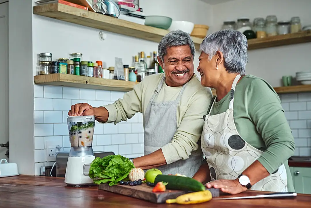 Photo of an elderly couple smiling in their kitchen while cooking a healthy meal