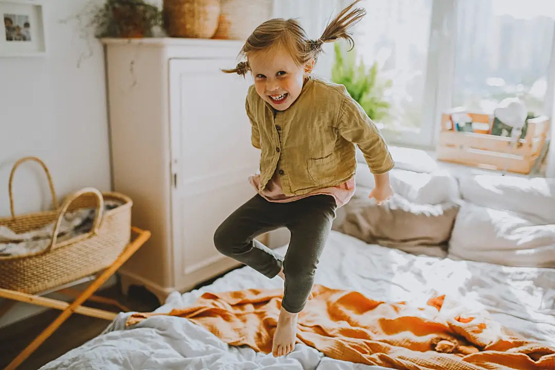 Photo of a girl smiling and jumping on a bed