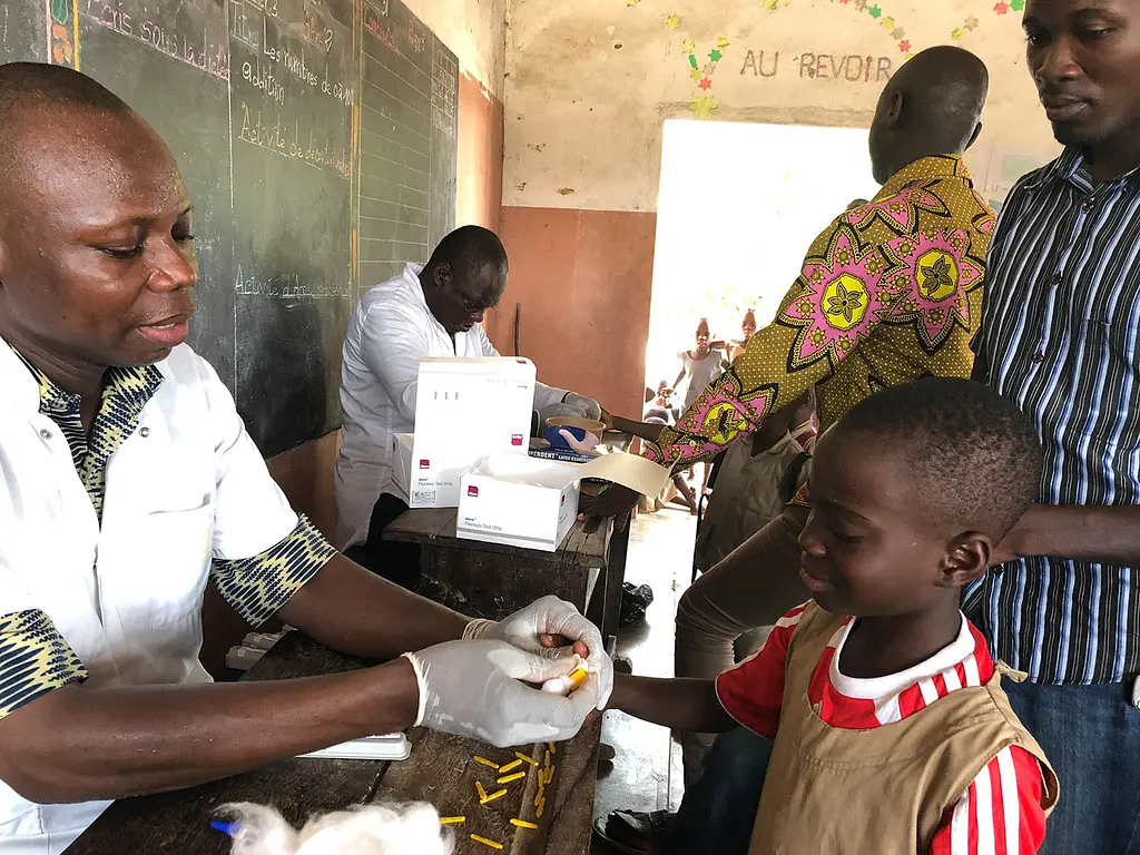 A young boy has his finger pricked during a transmission assessment survey for lymphatic filariasis at a school in Benin. Photo by Katie Zoerhoff for RTI International 
