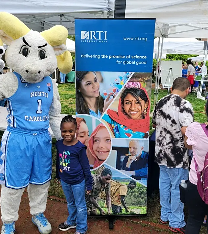 Photo of a child and the UNC mascot in front of an RTI banner at the UNC Science Expo