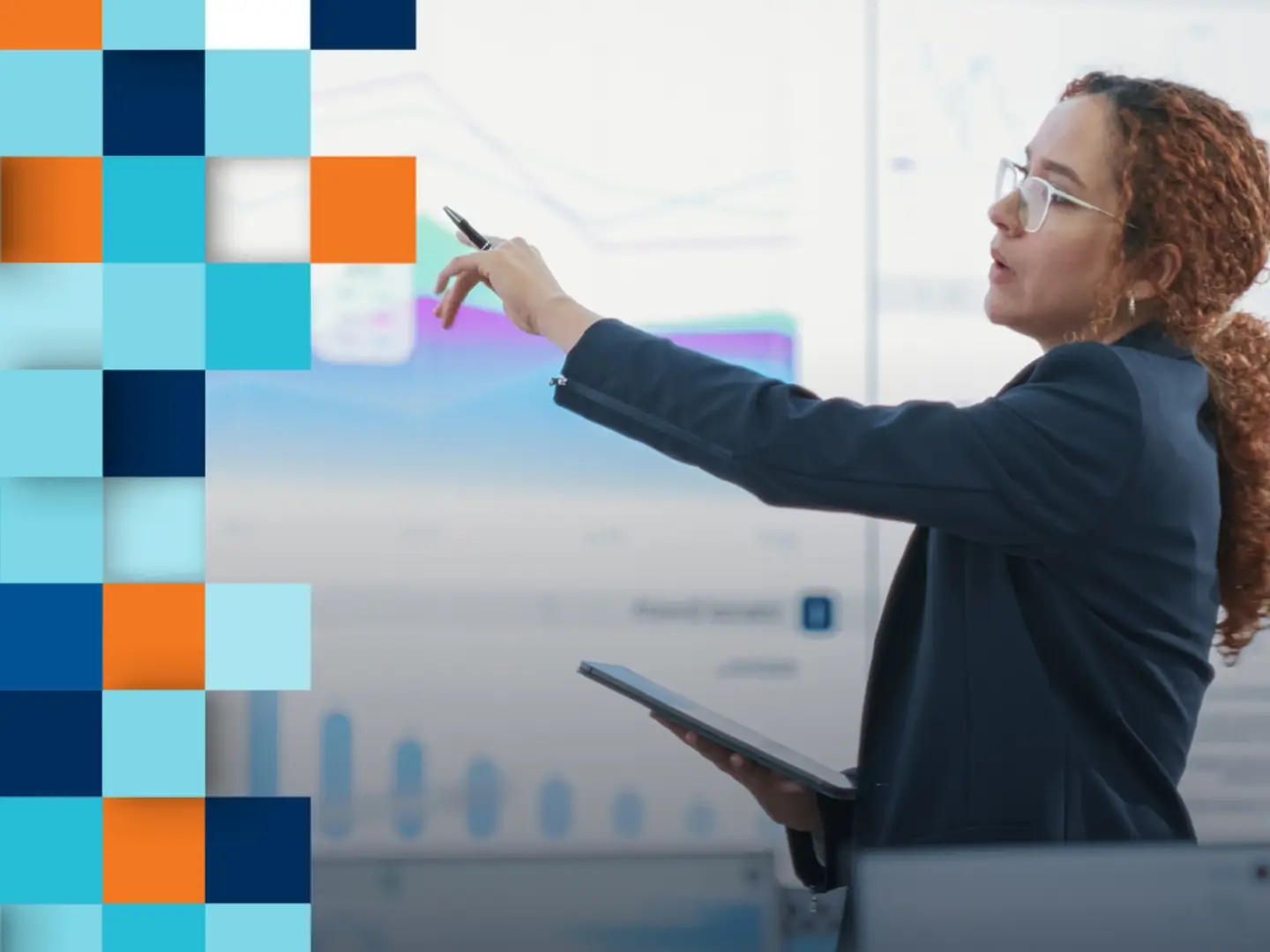 A businesswoman gestures with a pen while presenting data on digital screens behind her.